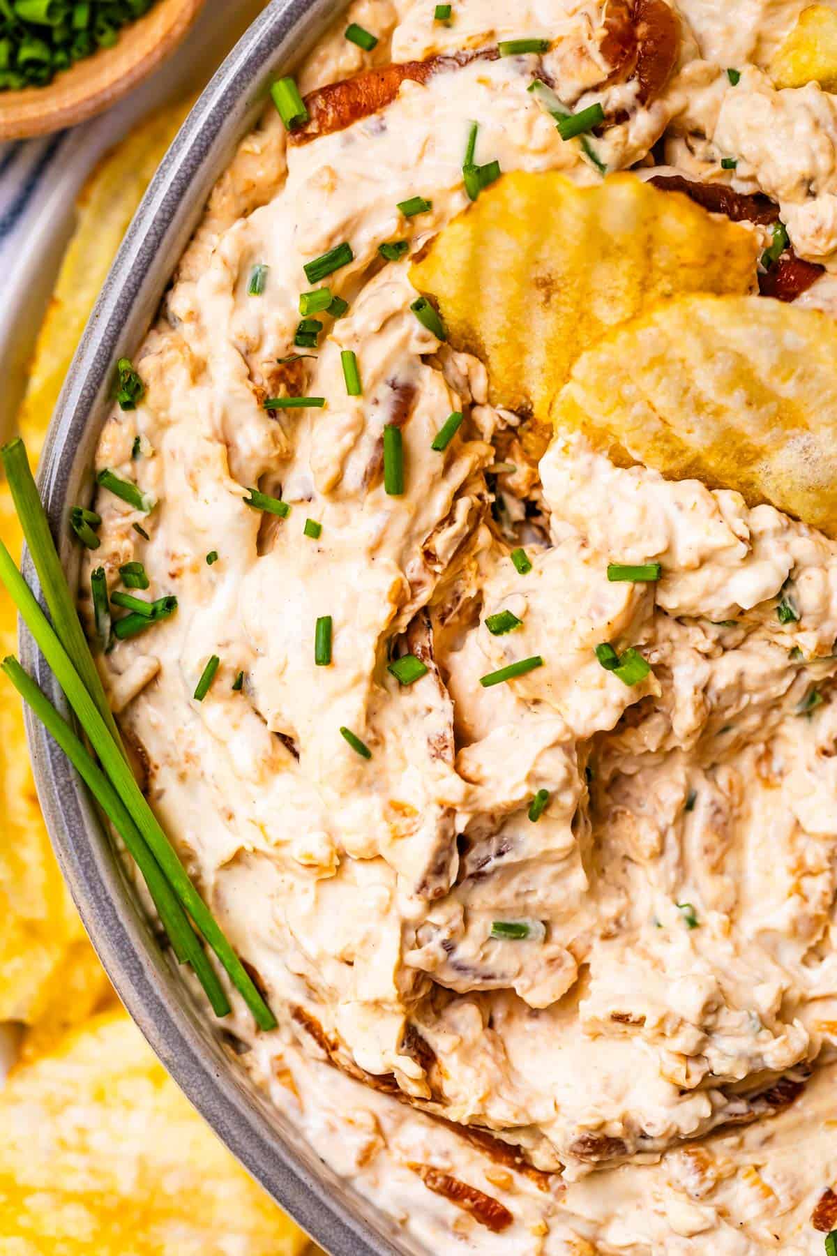 close up showing half a bowl filled with caramelized French onion dip with chive garnish and chips.