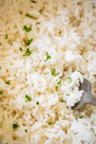 Close up of cooked white rice with parsley and a fork.