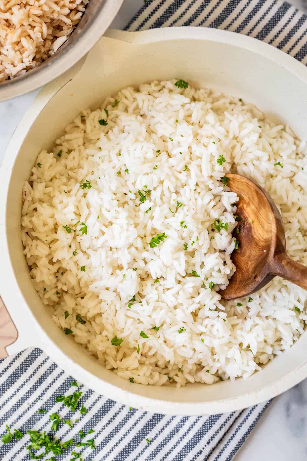 Cooked rice in a pot with wooden spoon and parsley.