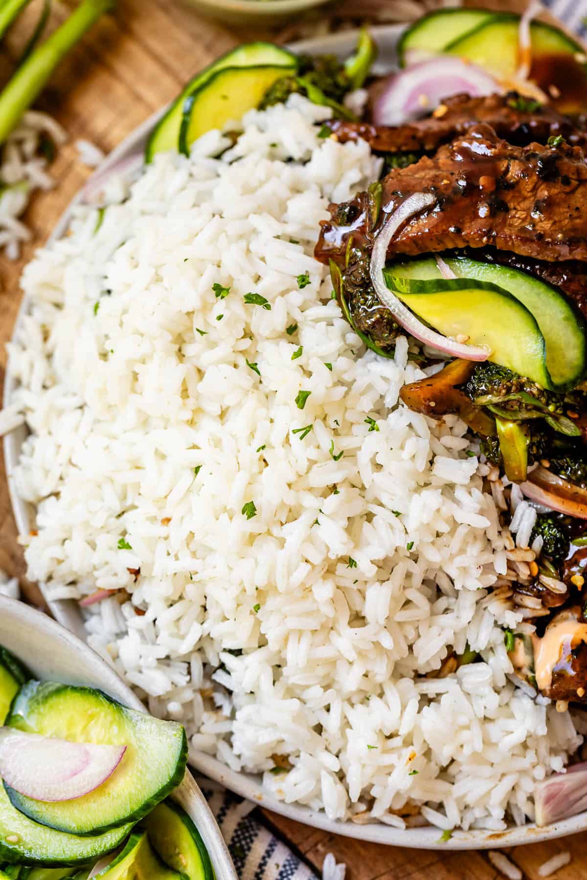 Cooked rice on plate with beef and broccoli and cucumbers.