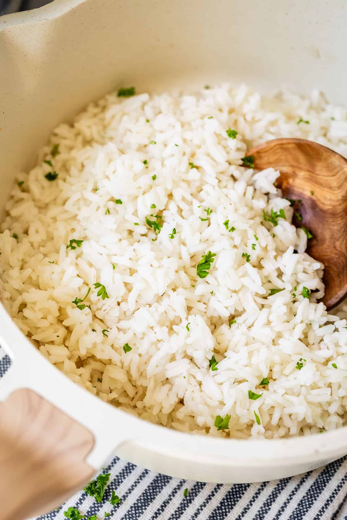 Cooked rice in white pot with wooden spoon and parsley.