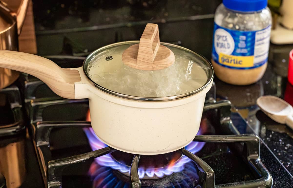 white pot of rice boiling on the stove with lid on.