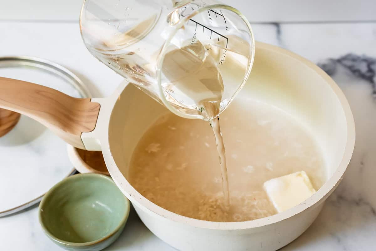 Preparing rice to cook on the stove by pouring water into pot with dry rice and butter.