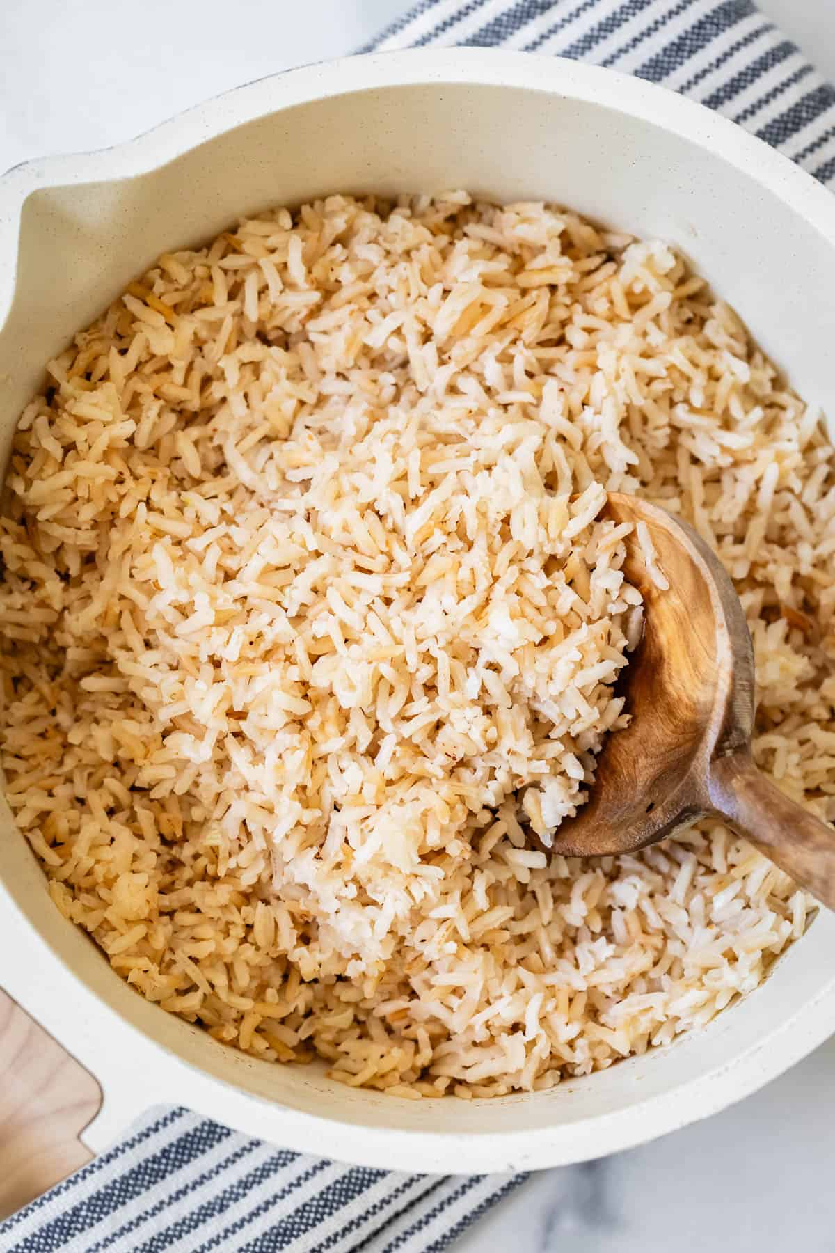 Rice cooked with browned butter in a white pot with a wooden spoon.