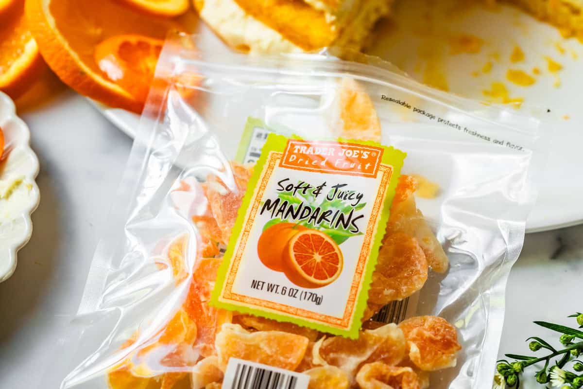 package of trader joes "soft & juicy mandarins" on top of a countertop with plated cake behind it.