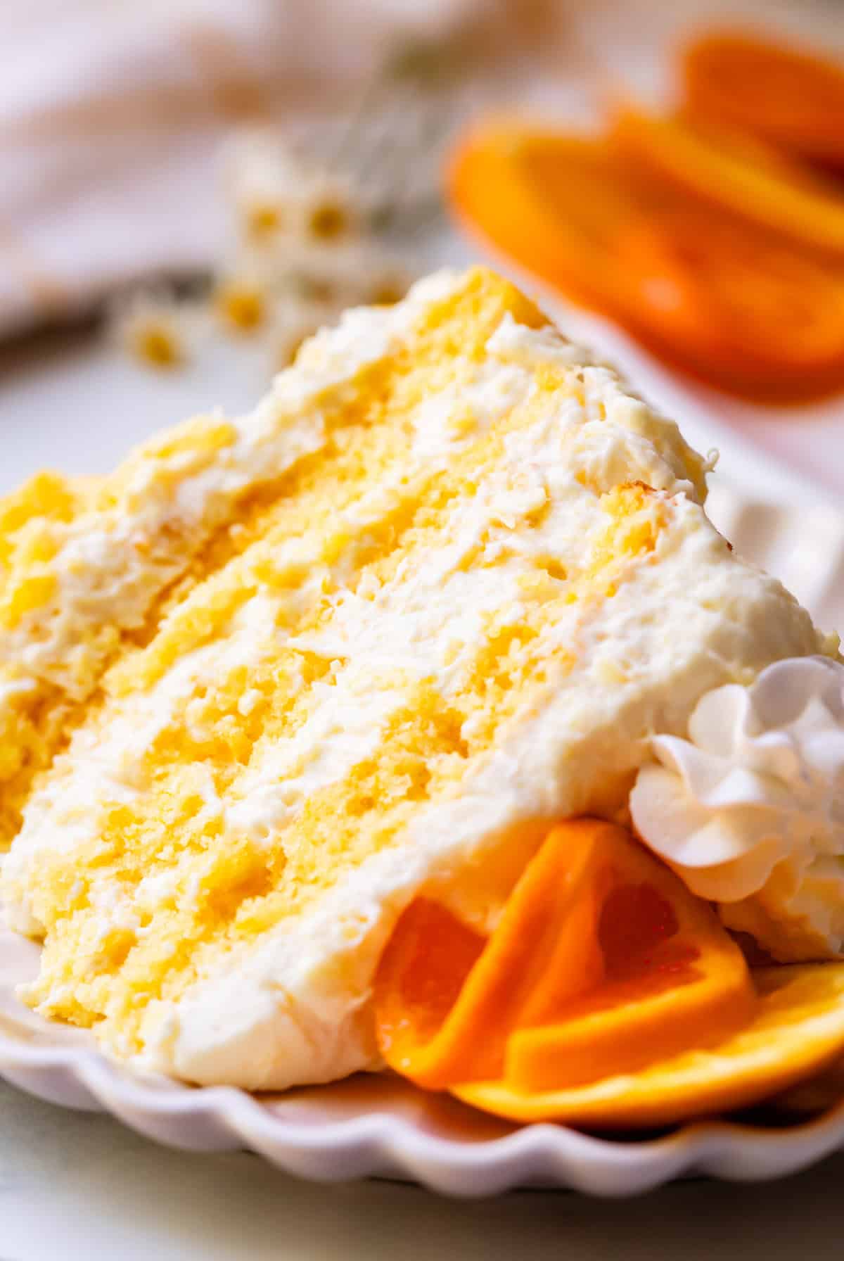 slice of caking lying on its side on a ceramic plate, with orange slices as garnish on top.
