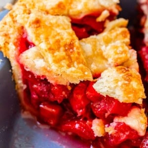 piece of lattice crust rhubarb and strawberry pie with lots of filling in a pie pan.
