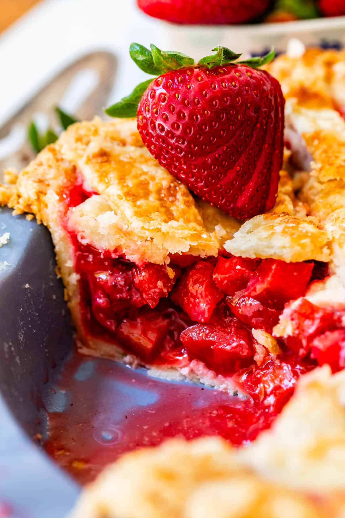 side view with all the strawberry rhubarb filling of a piece of pie in a pie pan with strawberry garnish.