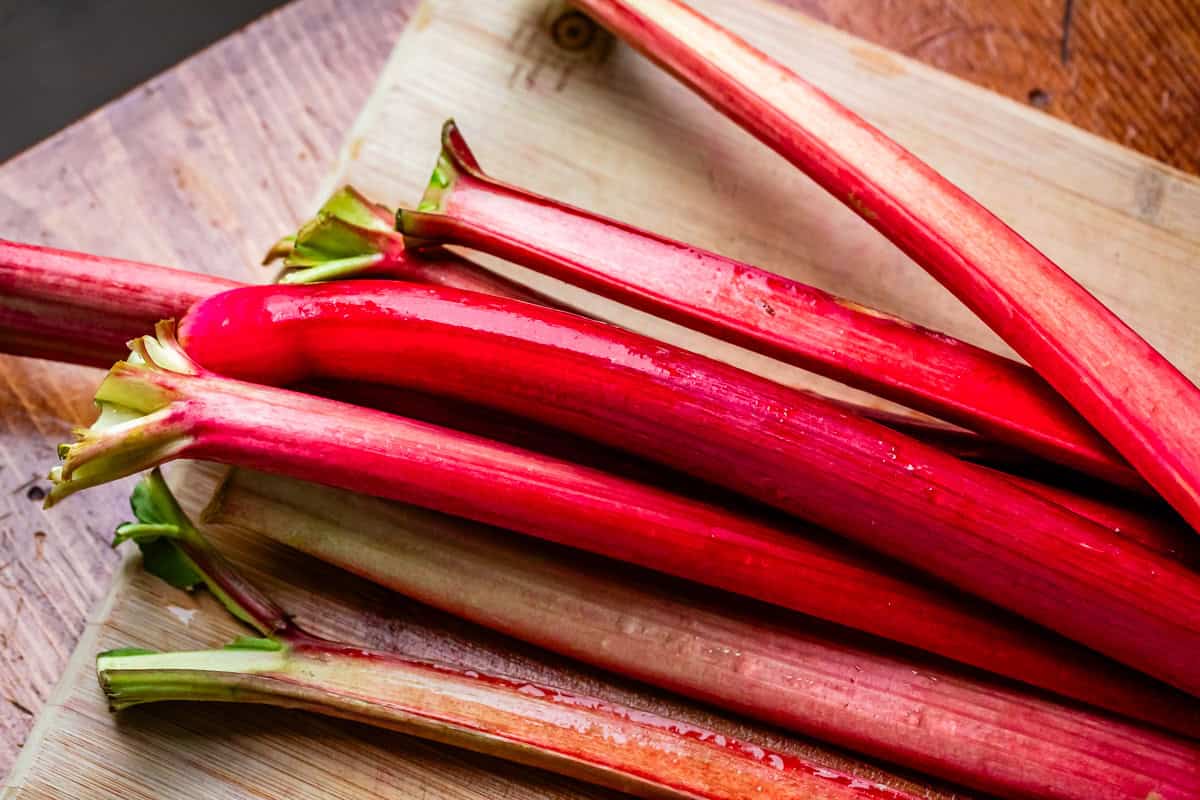 looking down at a bunch of about 7 or 8 whole stalks of rhubarb on a wooden cutting board.