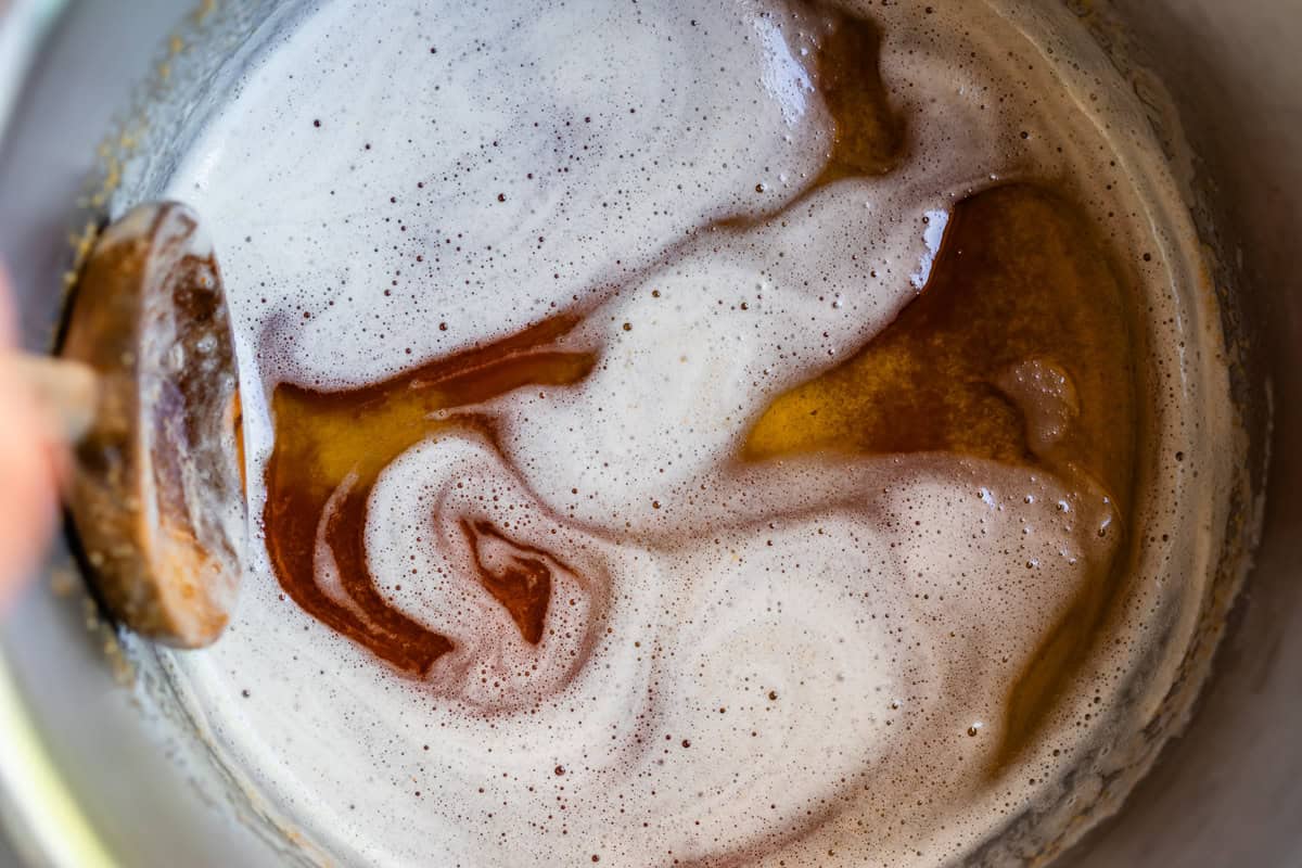 a wooden spoon in a metal pot stirring browned butter with light foam on top.