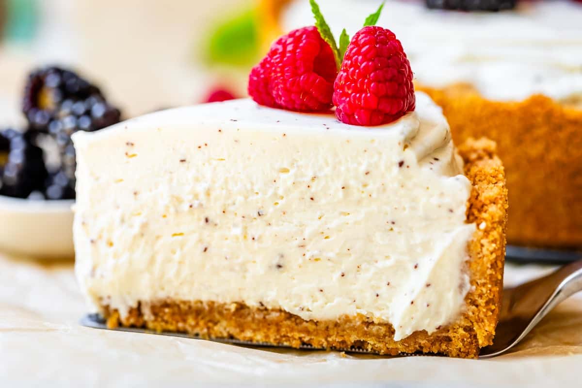 slice of perfectly cut no bake cheesecake with two raspberries on top on pie server.