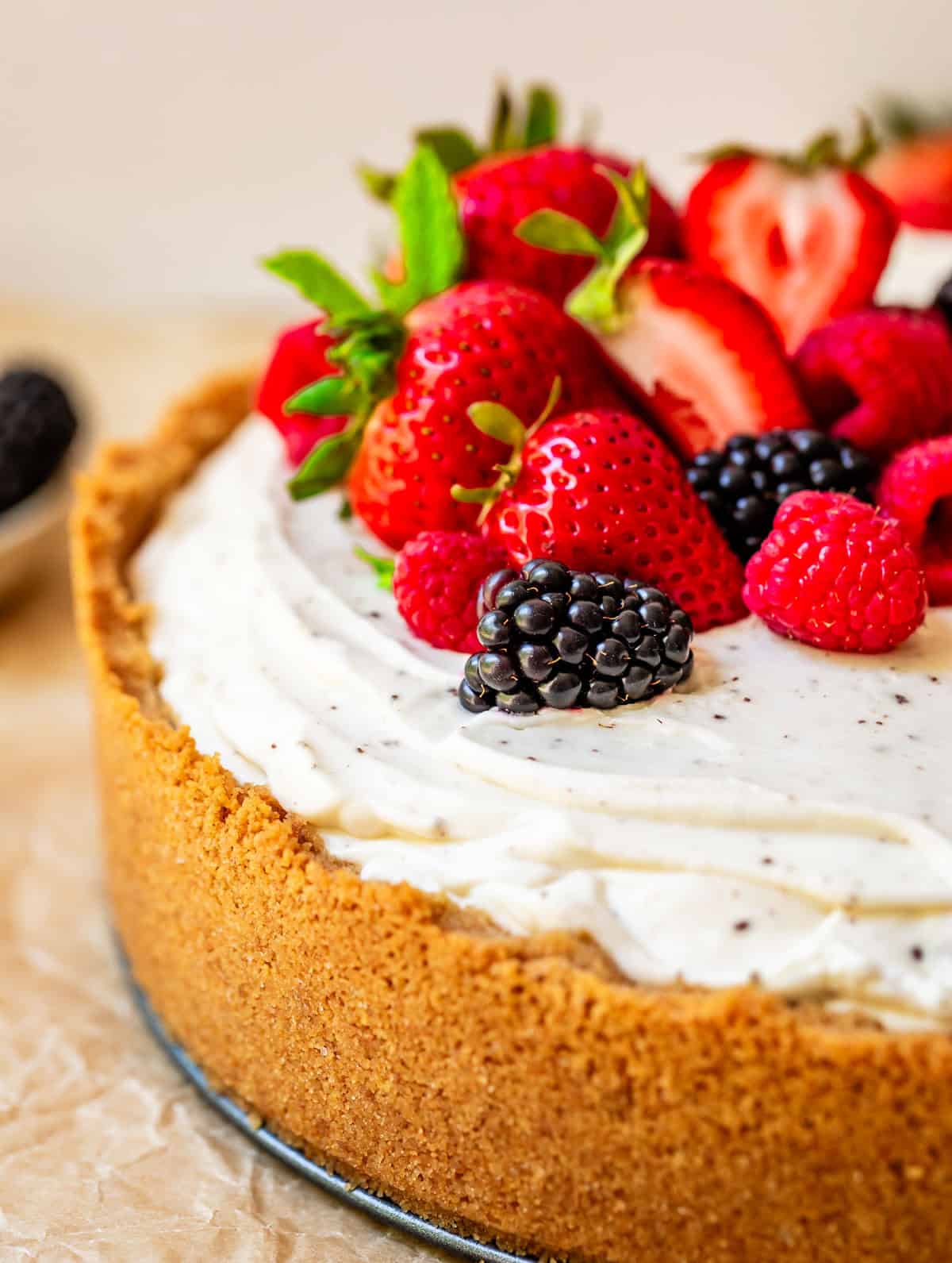 side view of whole no bake cheesecake showing sides of graham cracker crust and berry garnish.