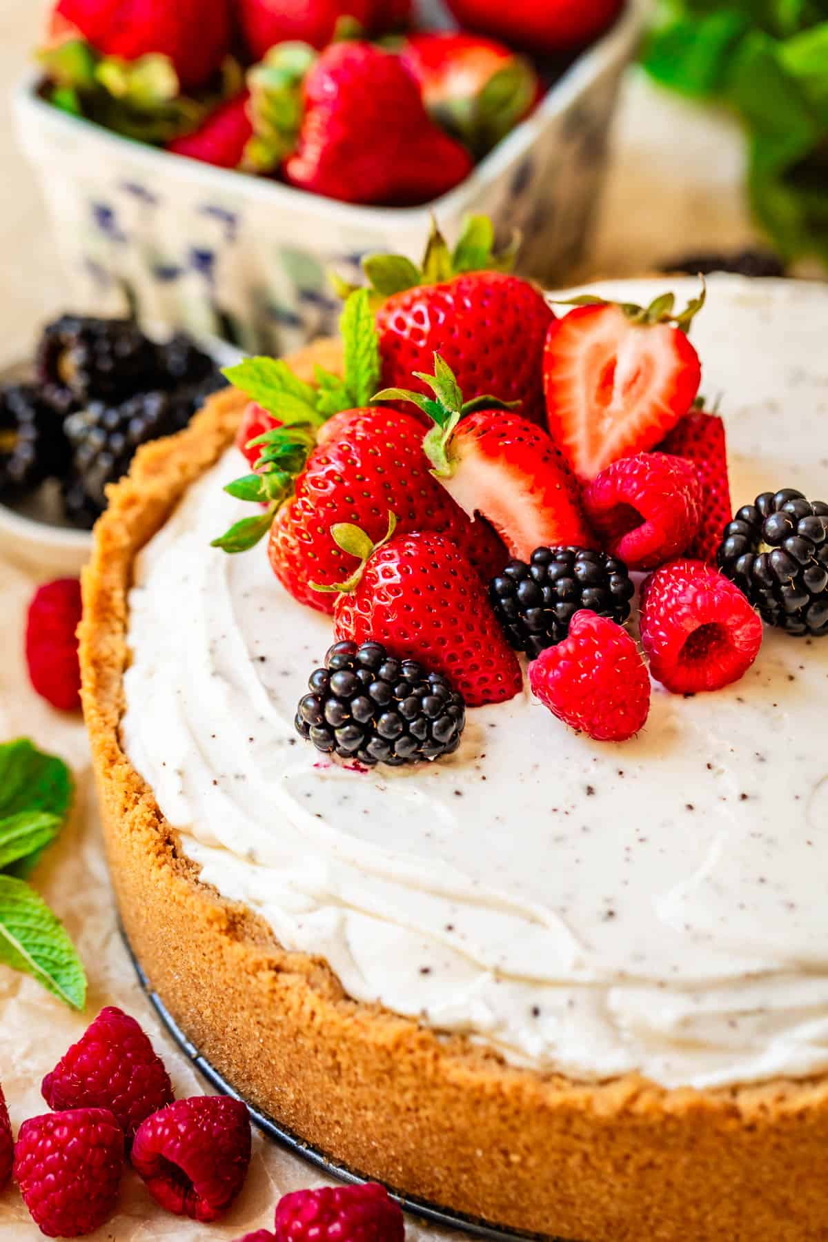 a released, whole no bake cheesecake with fresh strawberry, blackberry, and raspberry garnish.