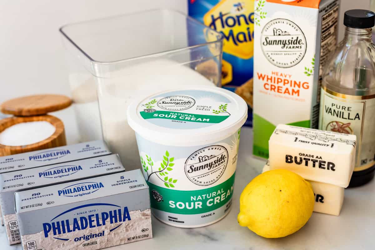 cream cheese, sugar, sour cream, lemon, butter, cream, crackers, vanilla, laid out on a marble counter.