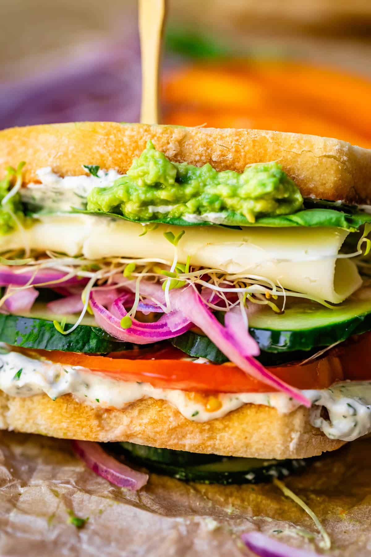 sideways view of a veggie sandwich with cheese showing all the layers and a skewr in the top.