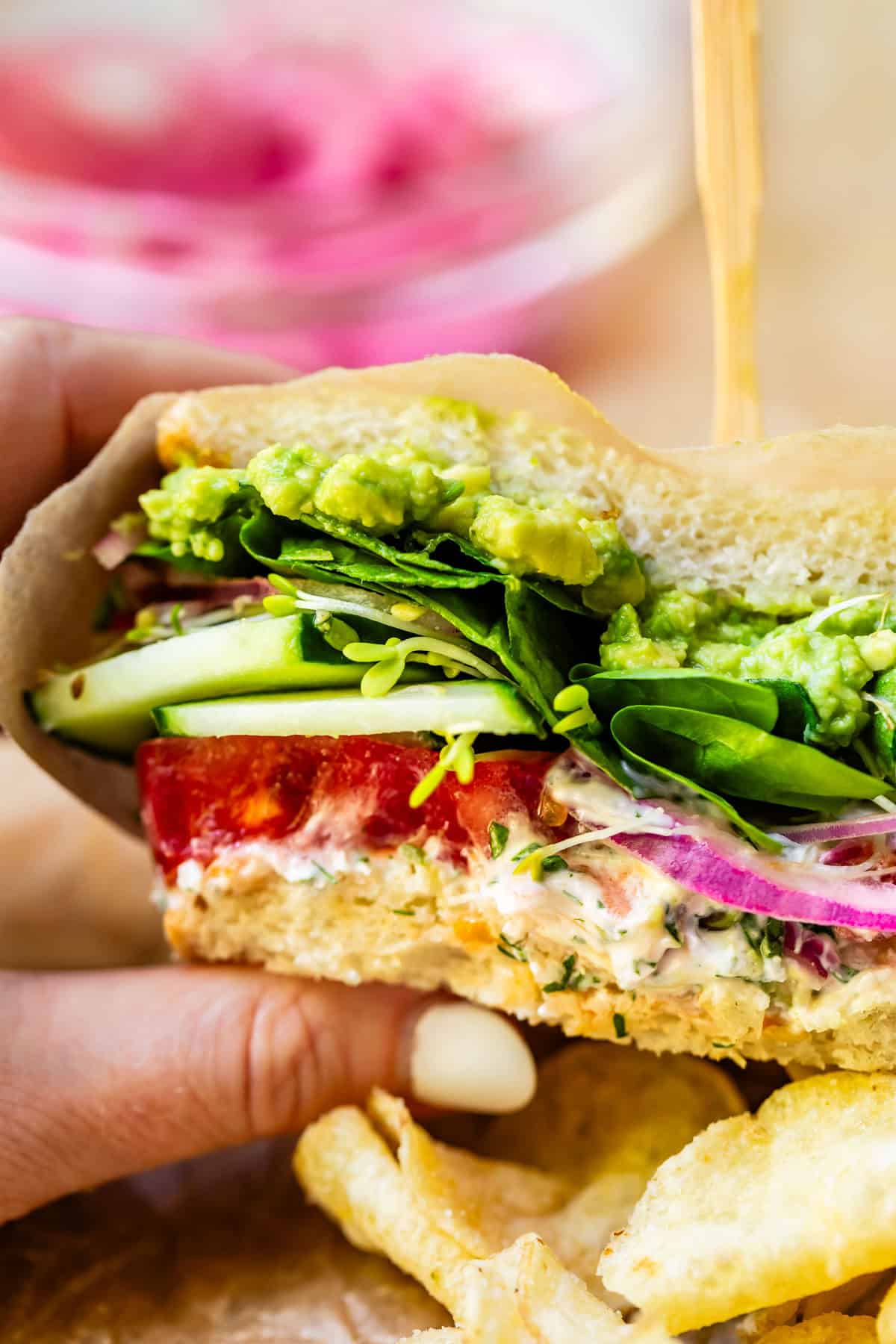 a hand holding a fresh veggie sandwich wrapped in parchment paper.