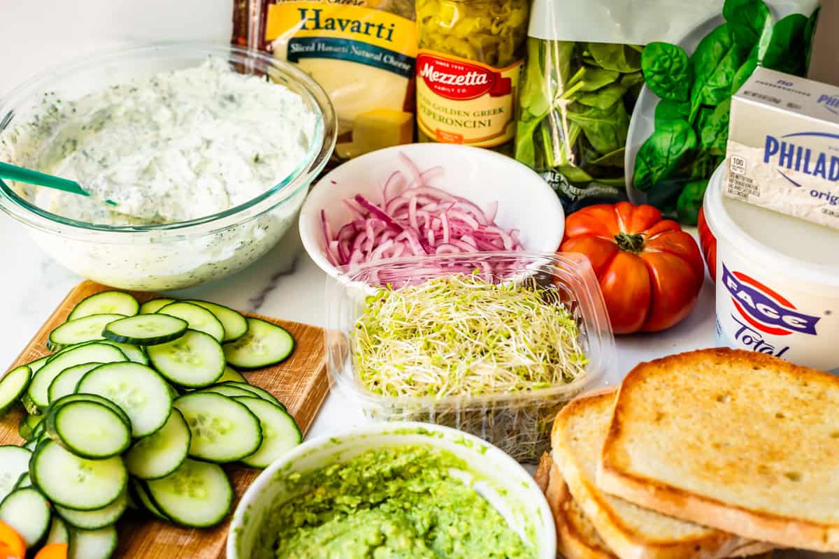 all ingredients for veggie sandwiches - spread, avocado, sourdough, and lots of veggies.