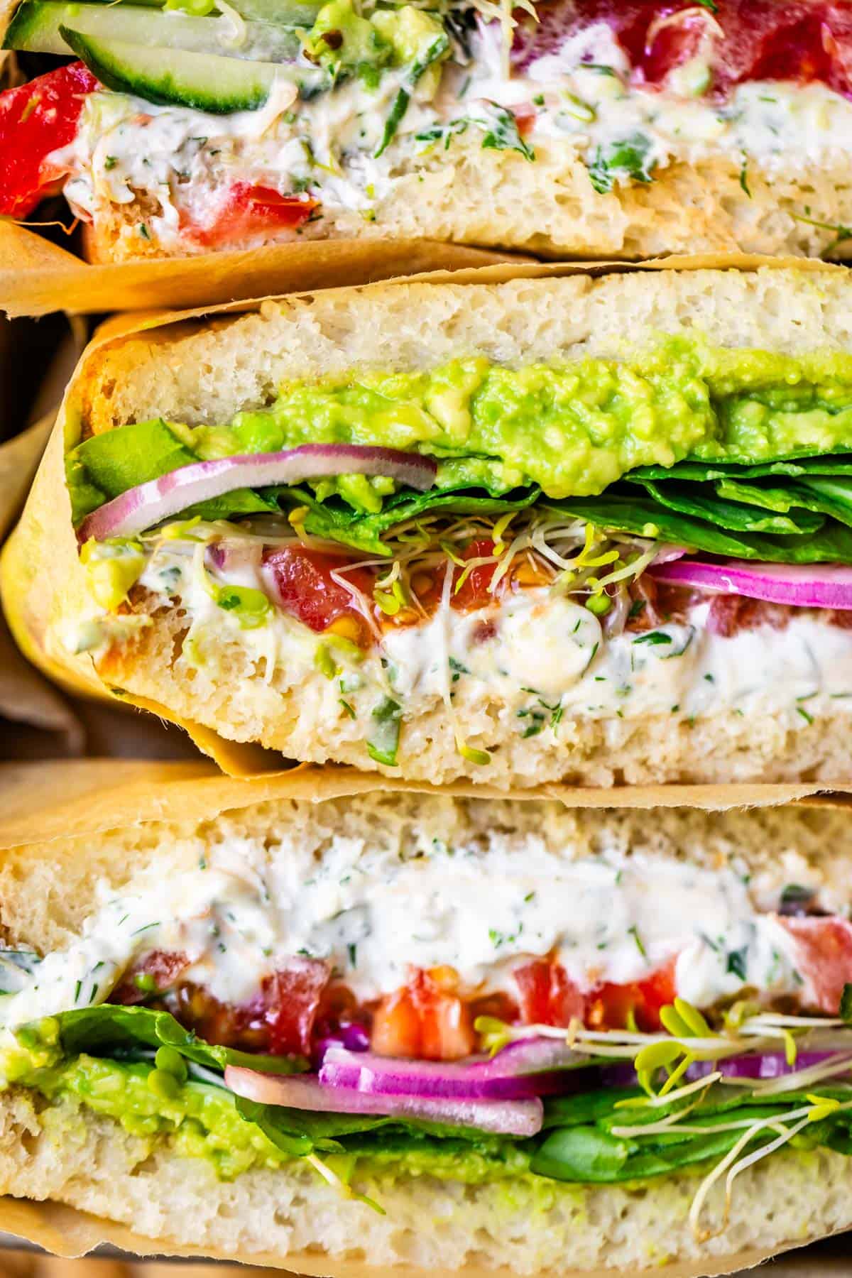 three veggie sandwiches wrapped in parchment paper stacked on top of each other.