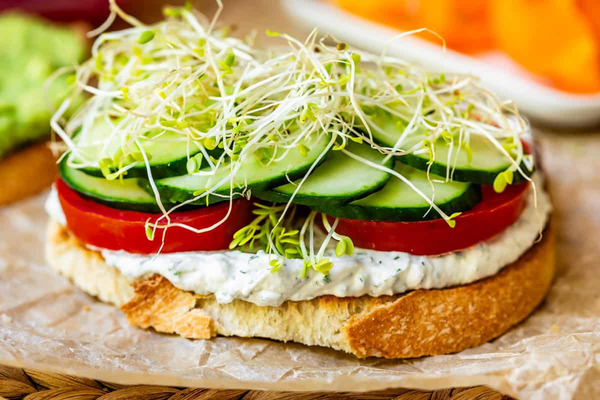 sourdough slice topped with creamy spread, tomato slices, cucumber slices, then sprouts.