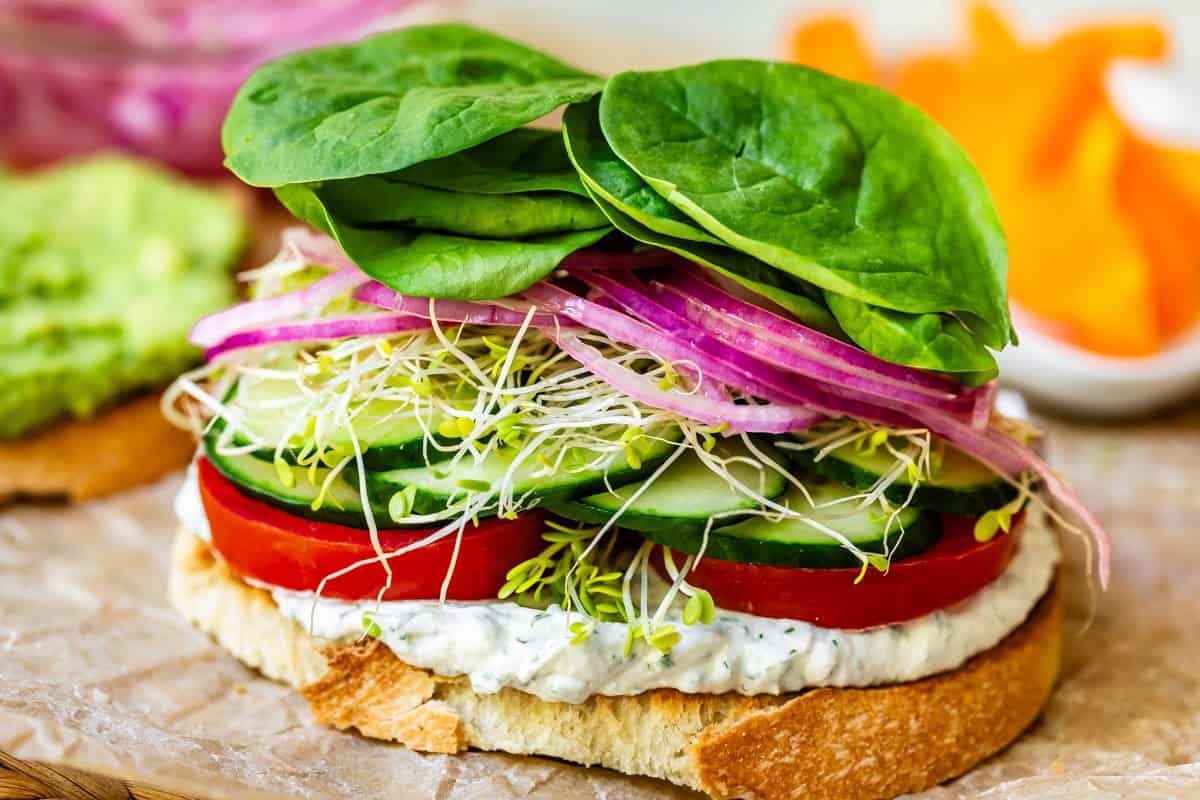 sourdough slice topped with spread, tomato, cucumber, sprouts, pickled onion, and spinach.
