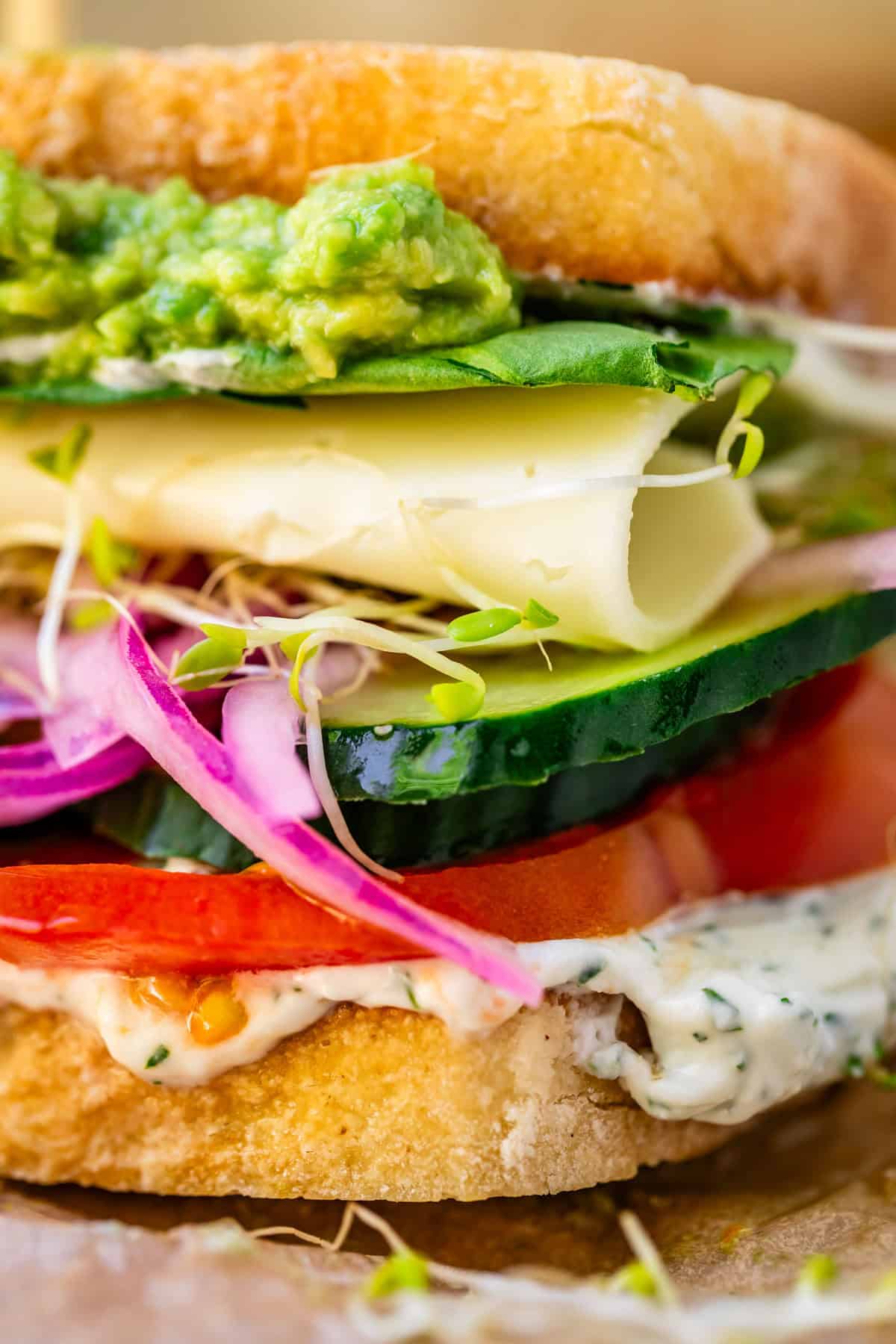veggie sandwich with spread, tomato, cucumber, onion, sprouts, cheese, and guac layers.
