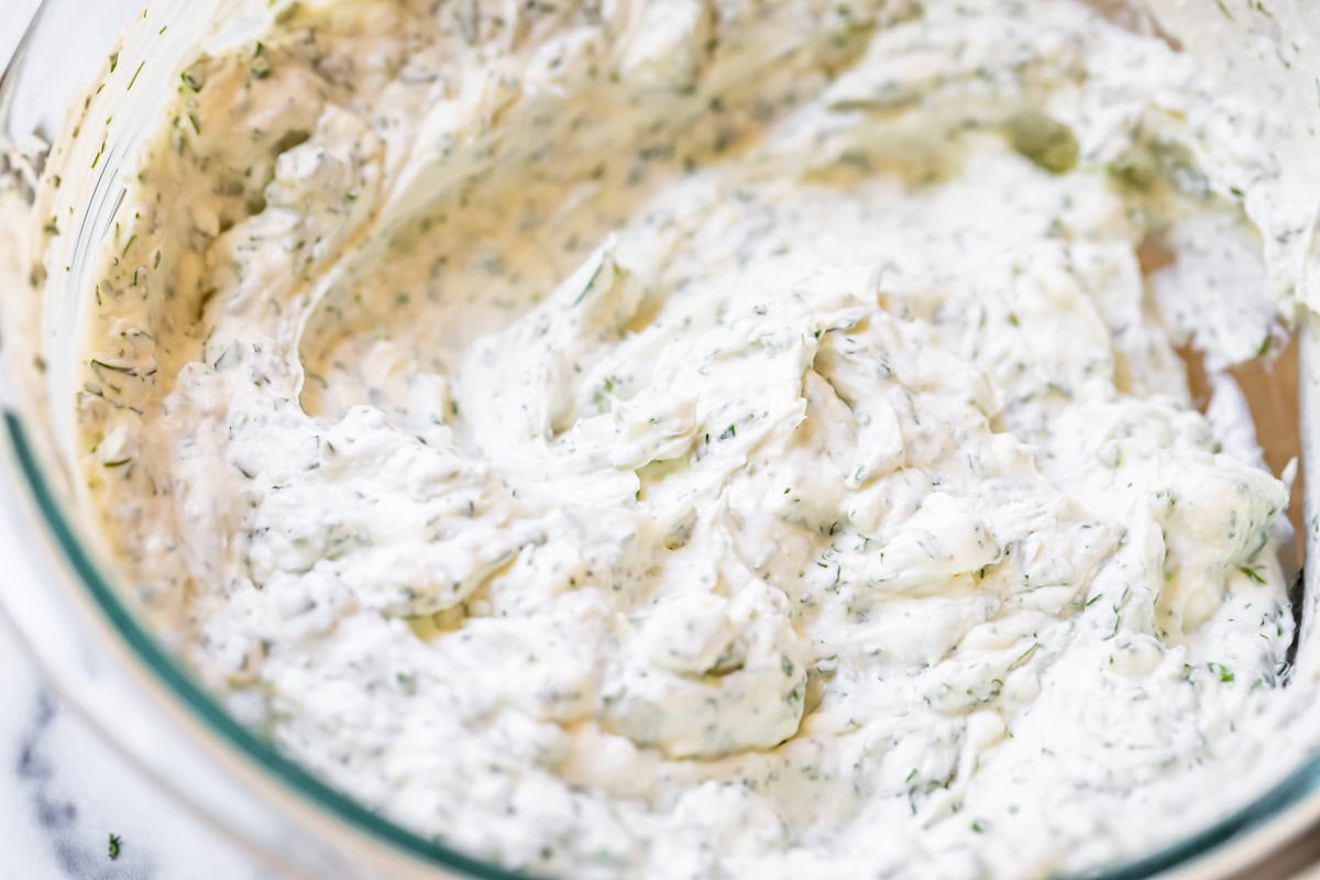 close up of creamy, herby cream cheese spread with dill and parsley in glass bowl.