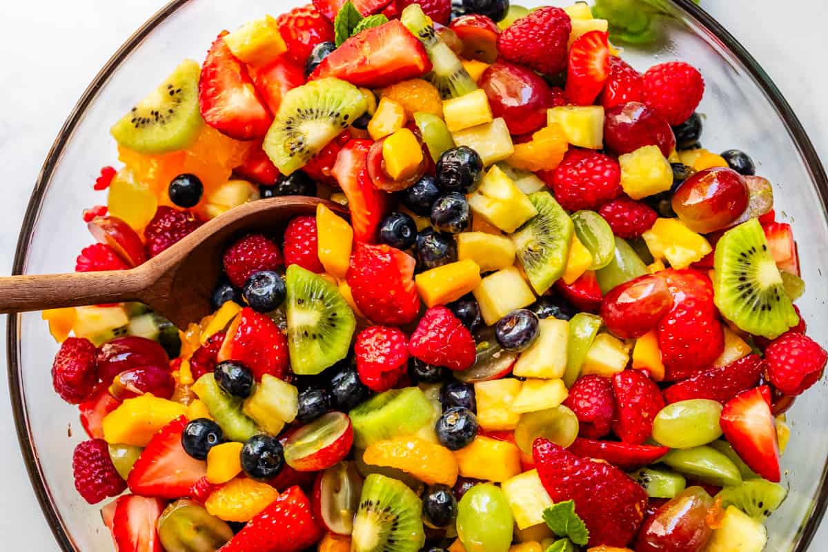 glass bowl with glazed fruit salad and wooden spoon stuck into the side.