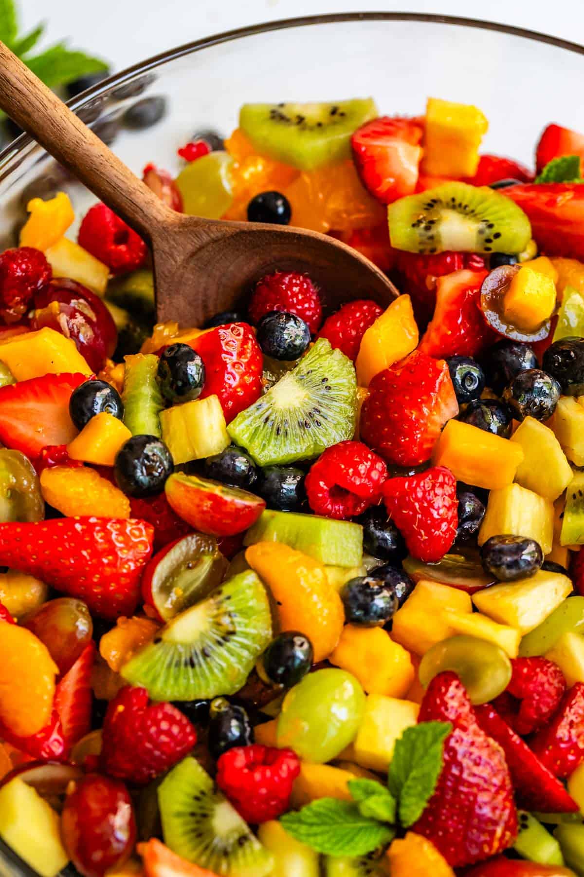 wooden spoon getting a scoop of fruit salad with glaze from a glass bowl.
