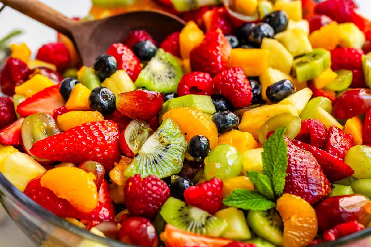 large wooden spoon stirring mixed fruit salad topped with a simple glaze.