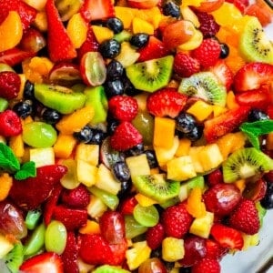 glass bowl of fruit salad with kiwi, grapes, strawberries, blueberries, mango, and more.