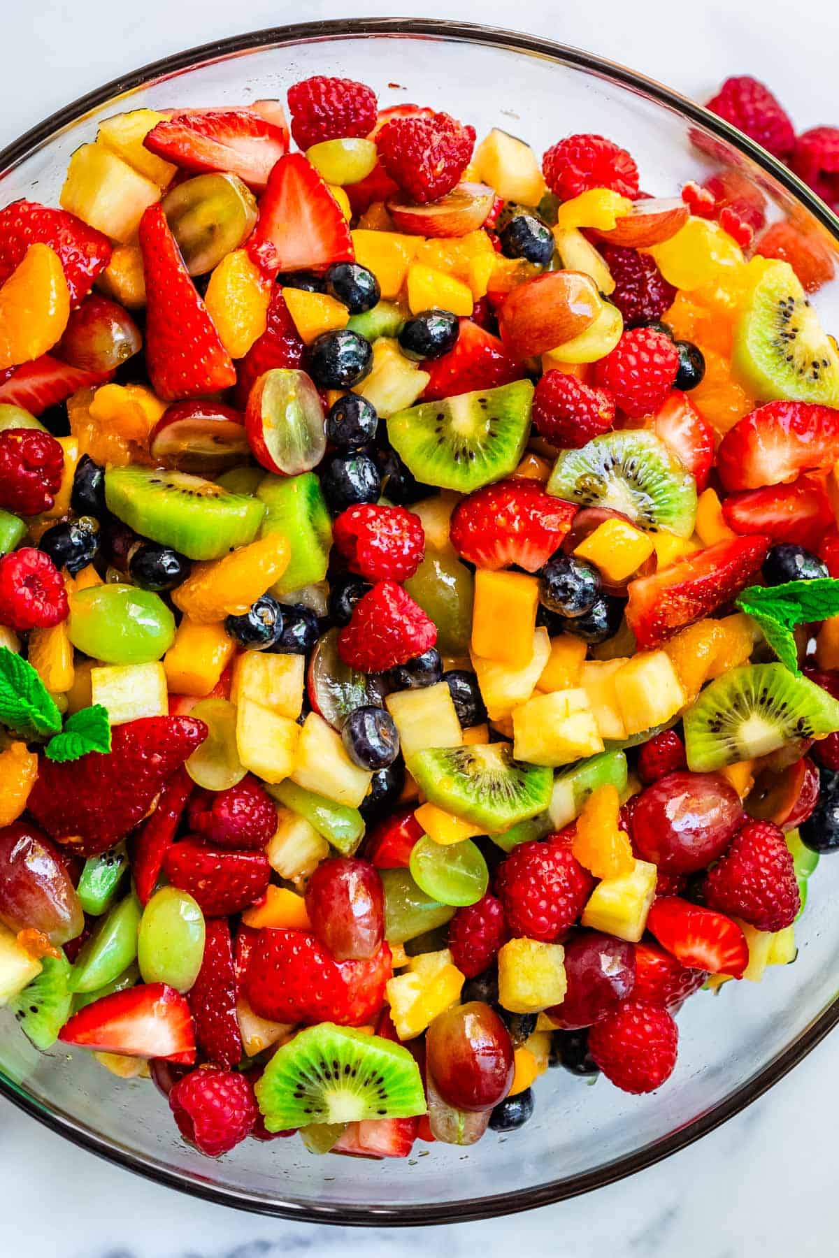 glass bowl of fruit salad with kiwi, grapes, strawberries, blueberries, mango, and more.