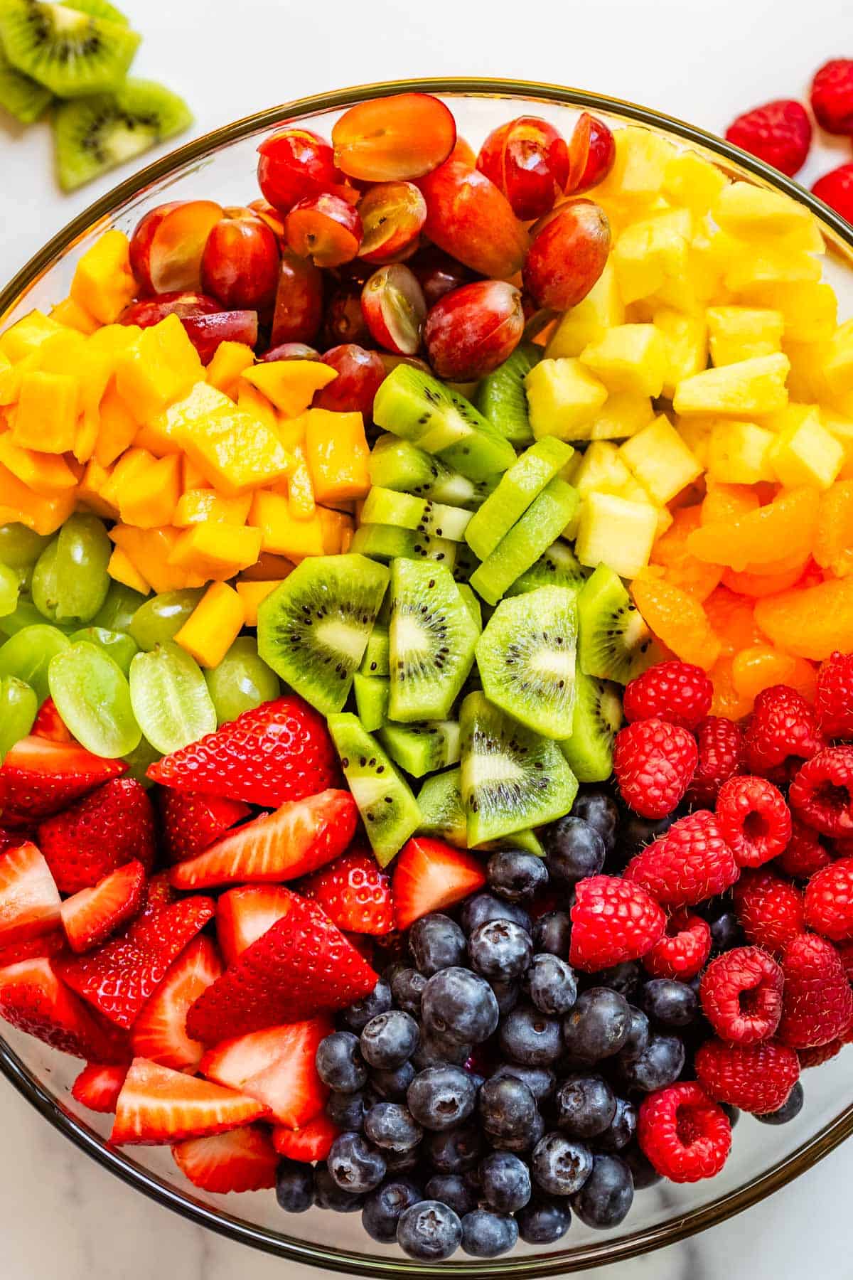 glass bowl filled to the brim with grapes, raspberries, strawberries, and more in fruit salad.