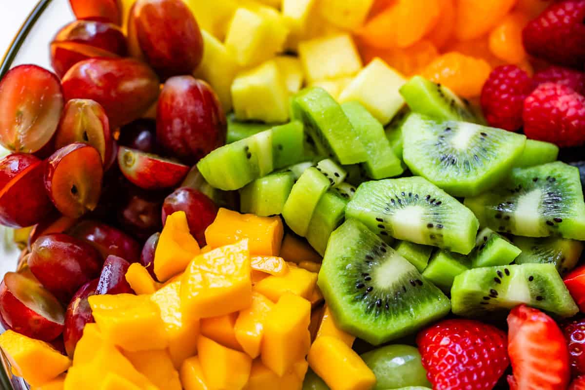 close up of cut up kiwi, mango, pineapple, strawberries, halved grapes, and raspberries.