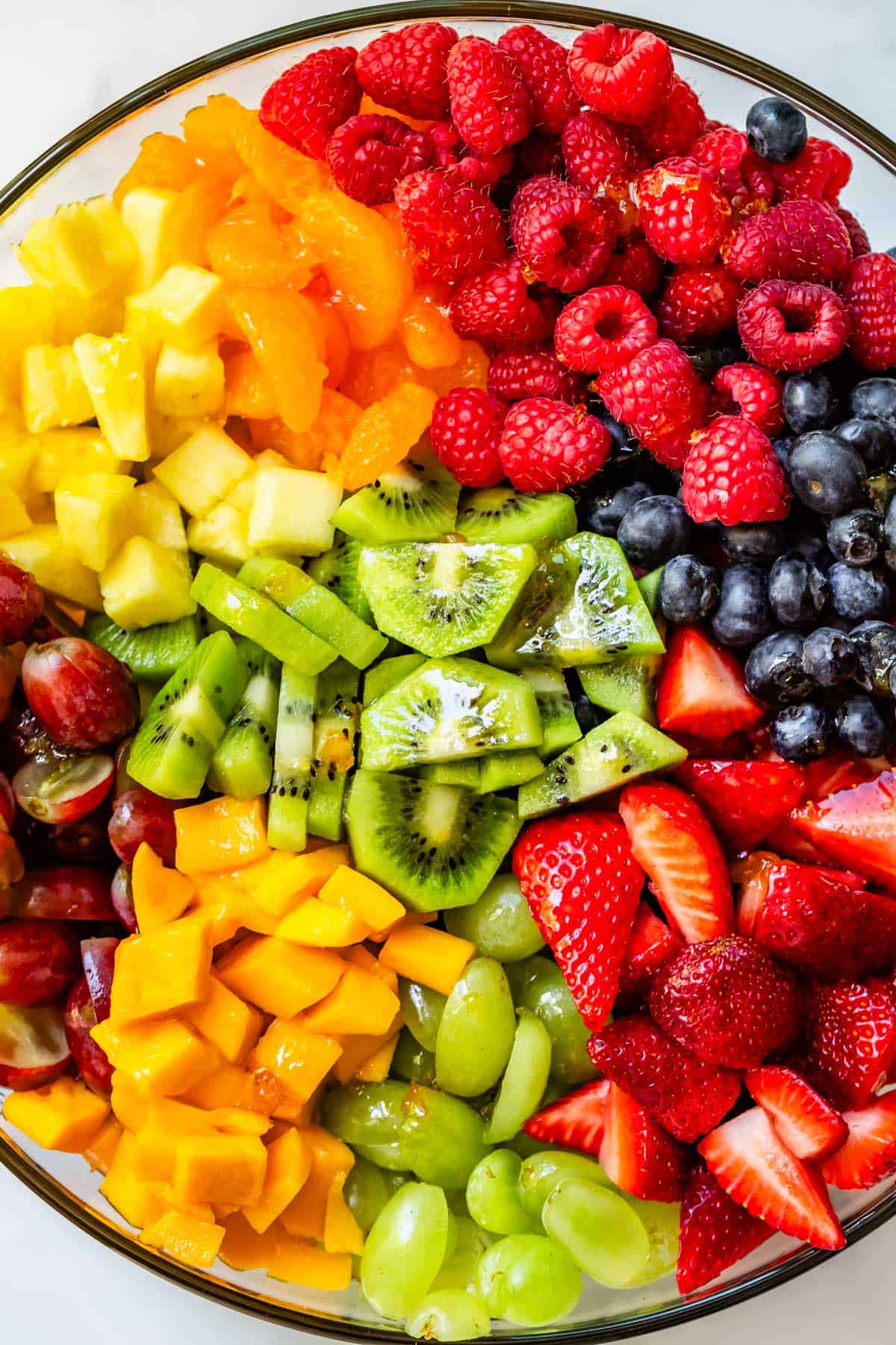 glass bowl filled with berries, kiwi, pineapple, mango, and grapes ready to be mixed.