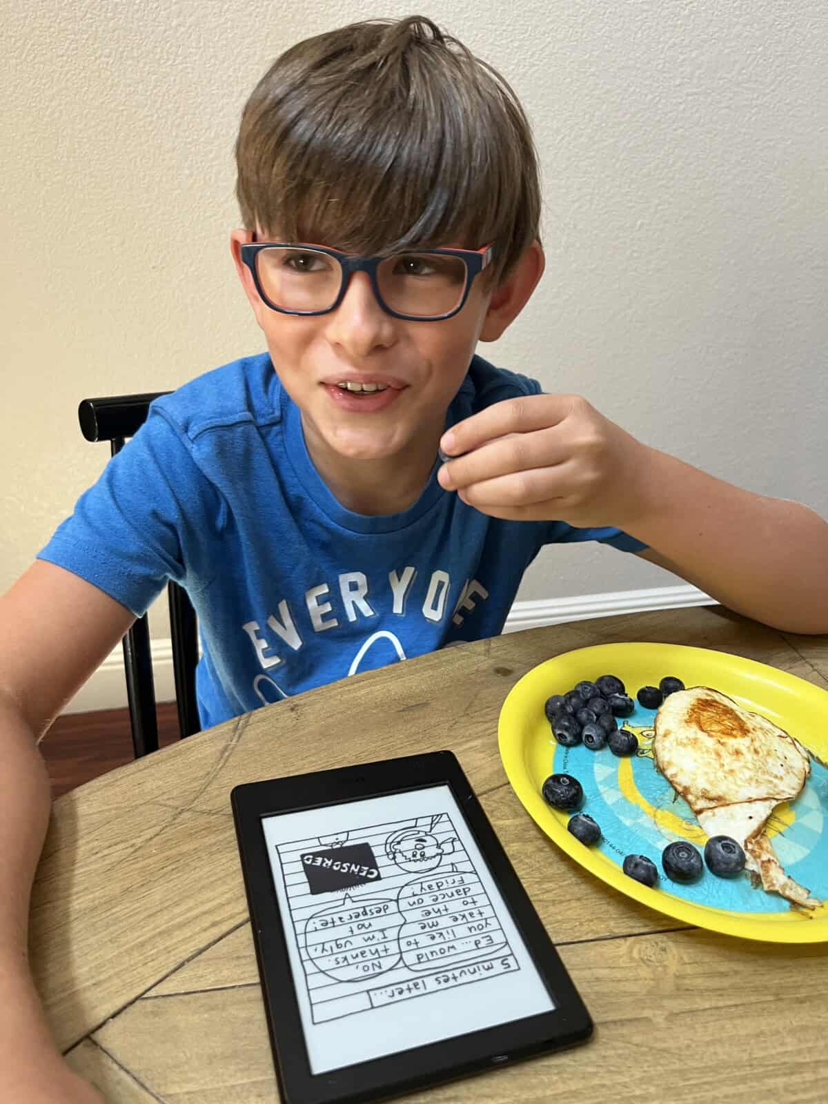 boy eating blueberries and an egg, reading a kindle.