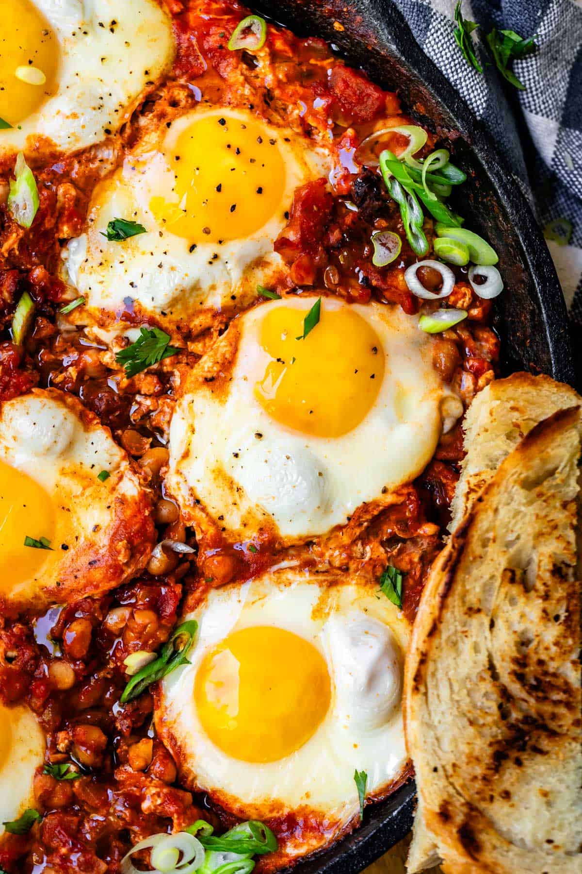 showing half a cast iron skillet with poached eggs in shakshuka sauce with bread on side.