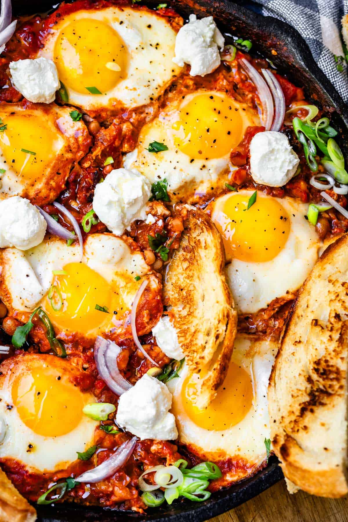 cast iron skillet with shakshuka, a piece of toast stuck into it, and red and green onion garnish.