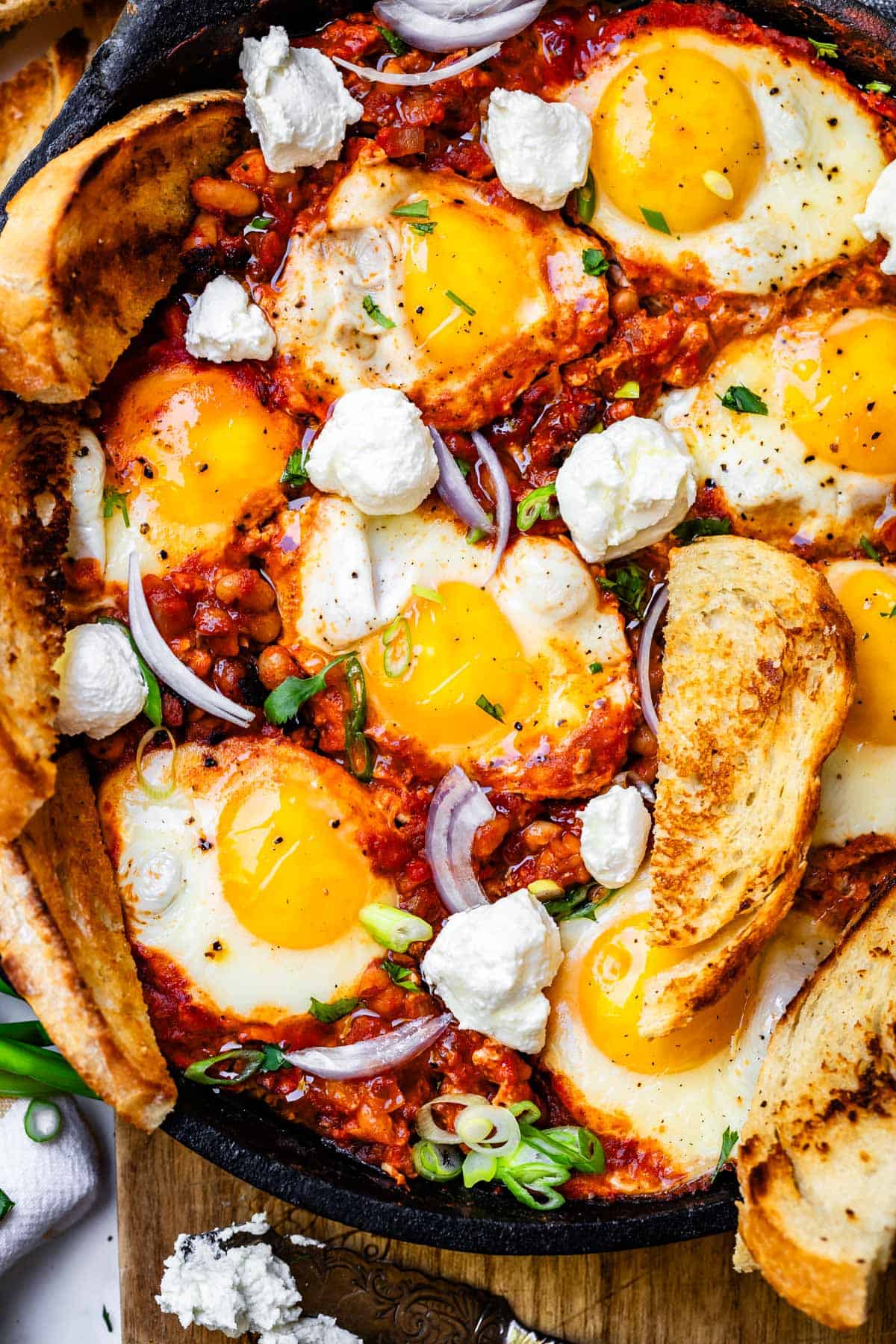 white bean shakshuka with dollops of goat cheese over the top and toast pieces along the edge of pan.