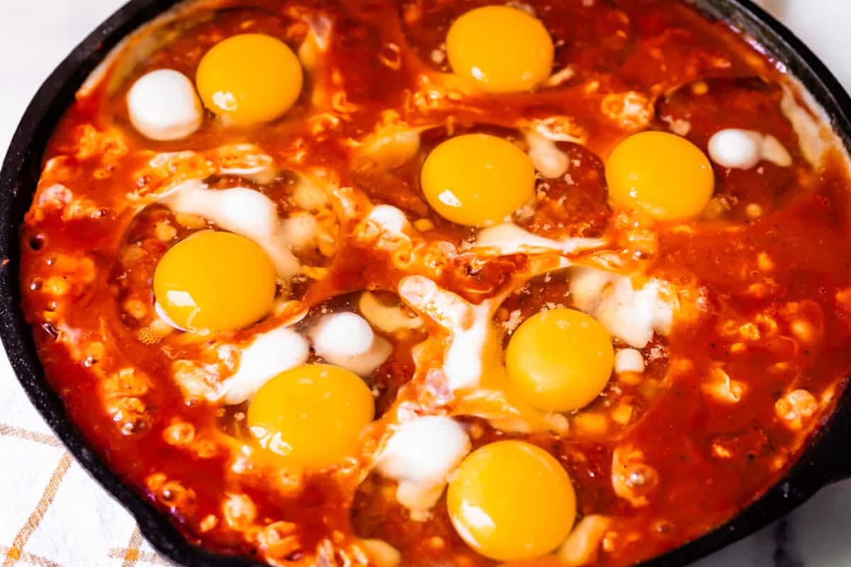 8 raw eggs nestled in the top of the sauce ready to be poached.