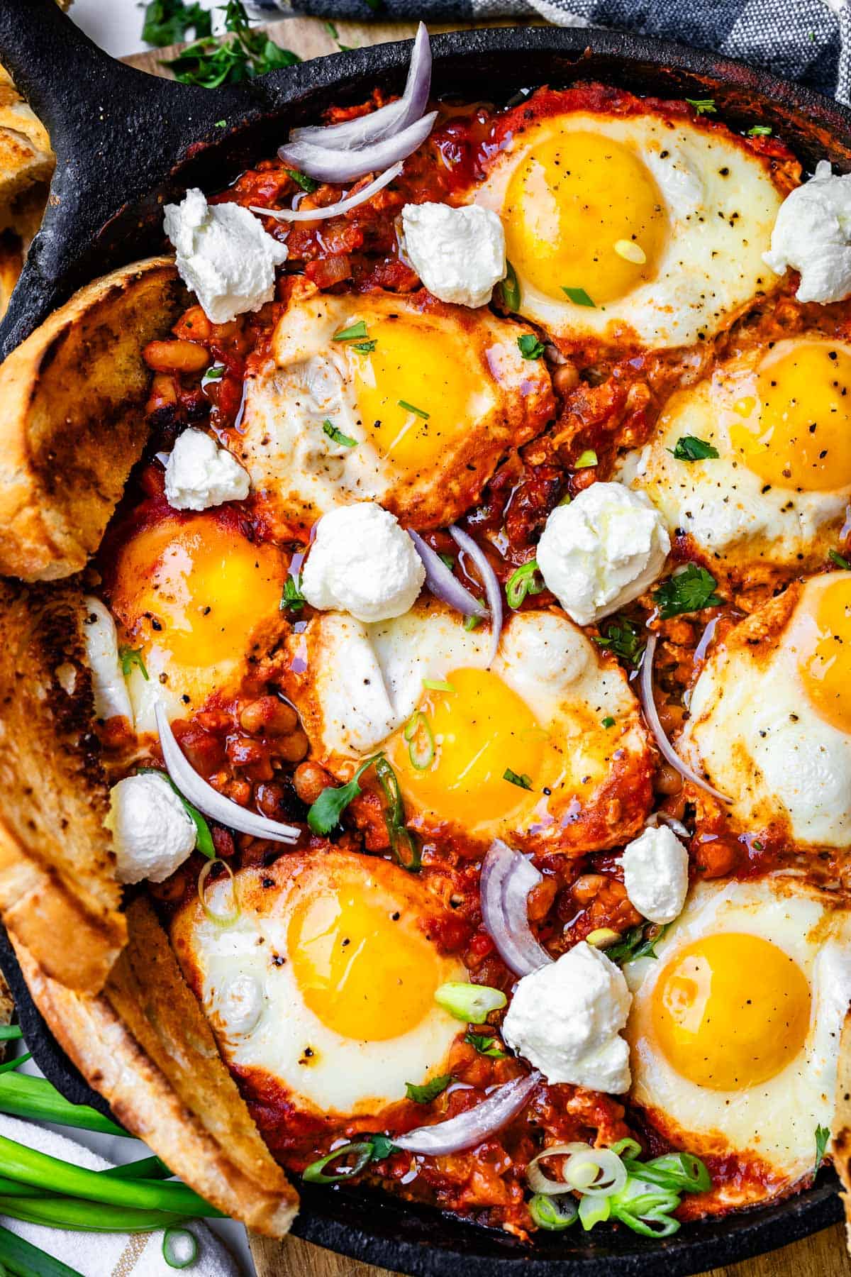 cast iron skillet filled with shakshuka with white beans and 8 poached eggs.