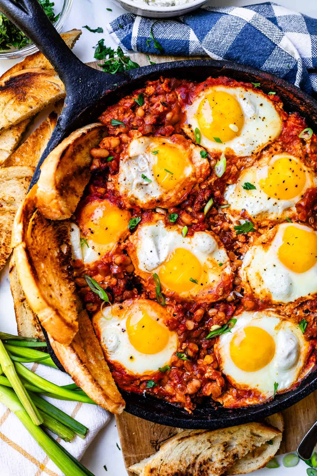 cast iron skillet with white bean shakshuka and 8 poached eggs, with three slices of toast.