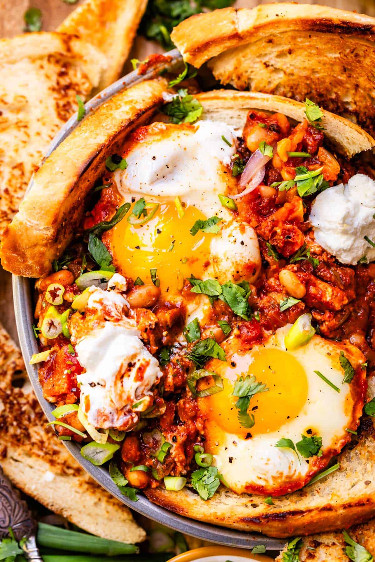 ceramic bowl filled with eggs and shakshuka sauce, and crusty pieces of bread surrounding it.