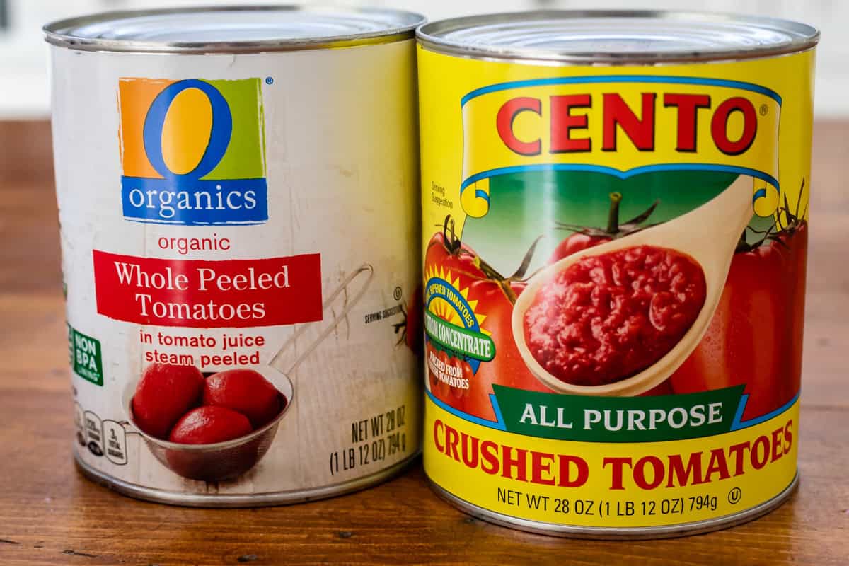 two 28 ounce cans of tomatoes, organics brand and cento brand, on a wood table