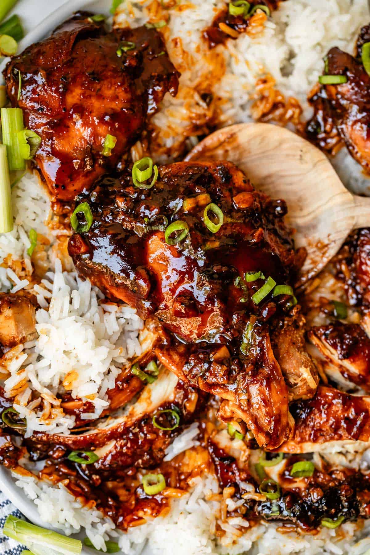 wooden spoon picking up a chicken thigh topped with honey garlic sauce.