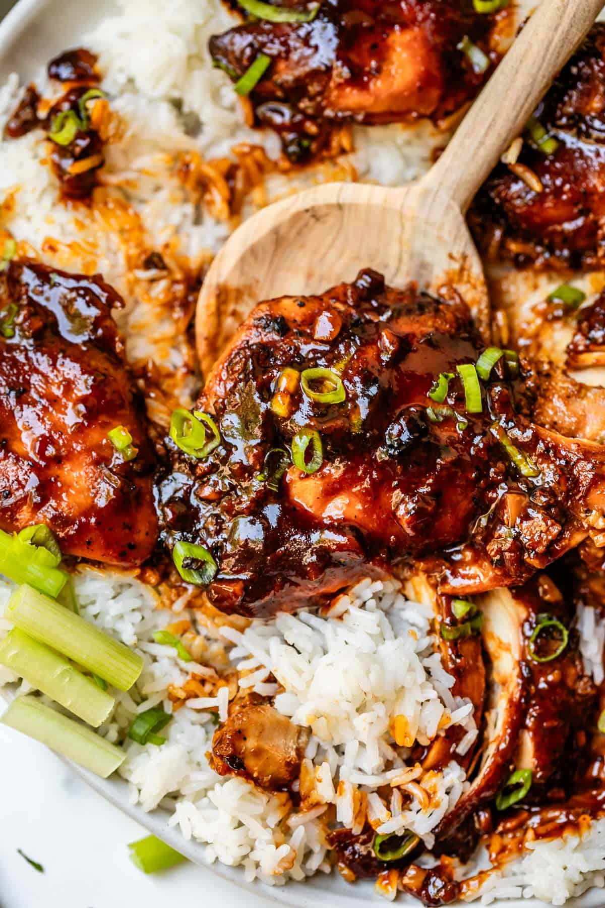 wooden spoon scooping a honey garlic chicken thigh from a bed of white rice.