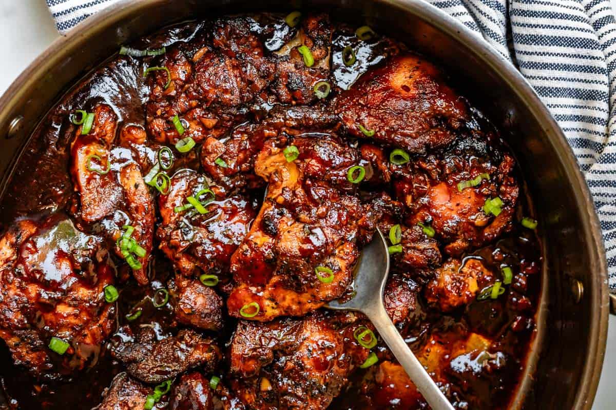 spoon serving from pot full of honey garlic chicken with green onion garnish.