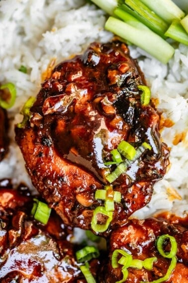 one chicken thigh in honey garlic sauce with green onion topping on top of white rice.