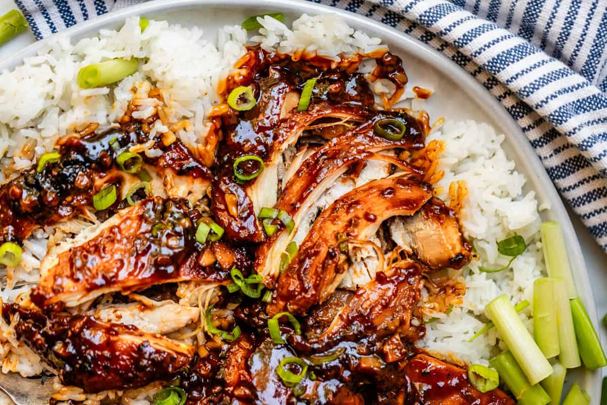 shredded honey garlic chicken garnished with green onion over white rice.