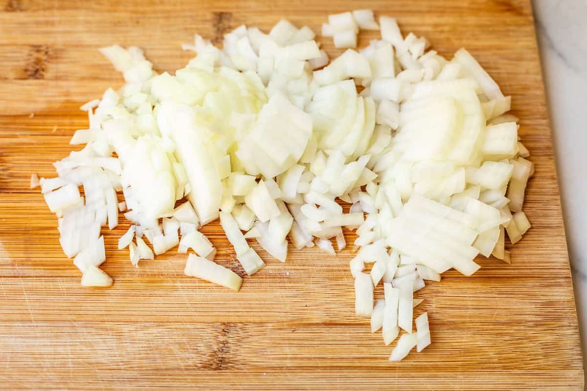 a whole onion, chopped, on a wooden cutting board that is set on a countertop.