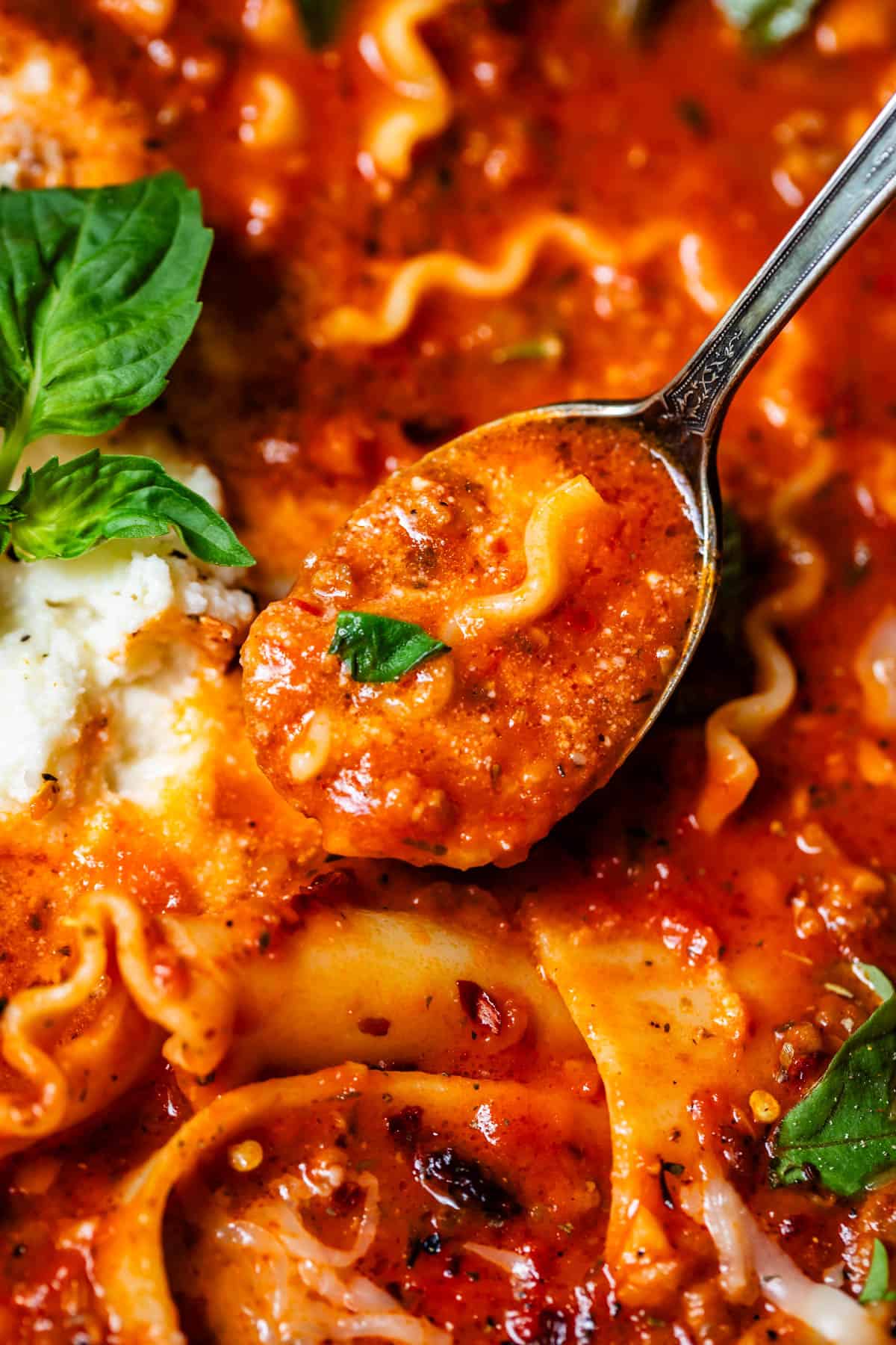 metal spoon holding a scoop of marinara broth and part of a noodle from lasagna soup.